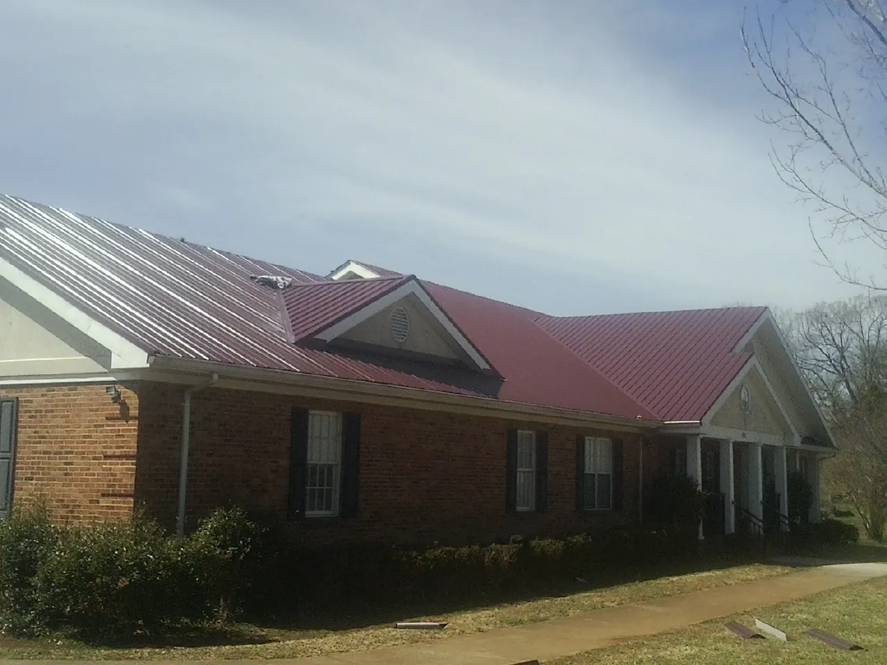 Red metal roof with gabled entries on a long brick building, from a Hail Damage Roof Repair job in Lancing