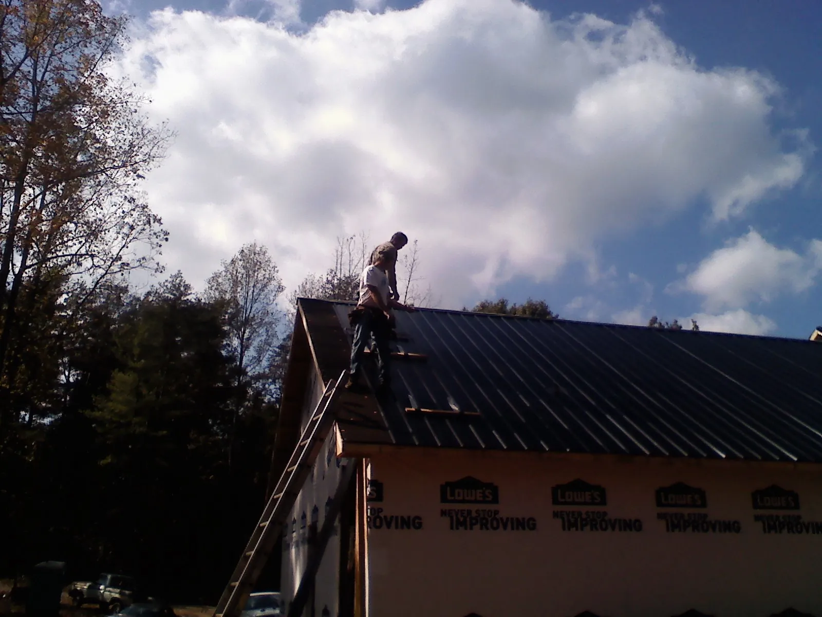 Roofer fastening dark metal panels high against a cloudy sky, from a Roof Inspection job in Lancing