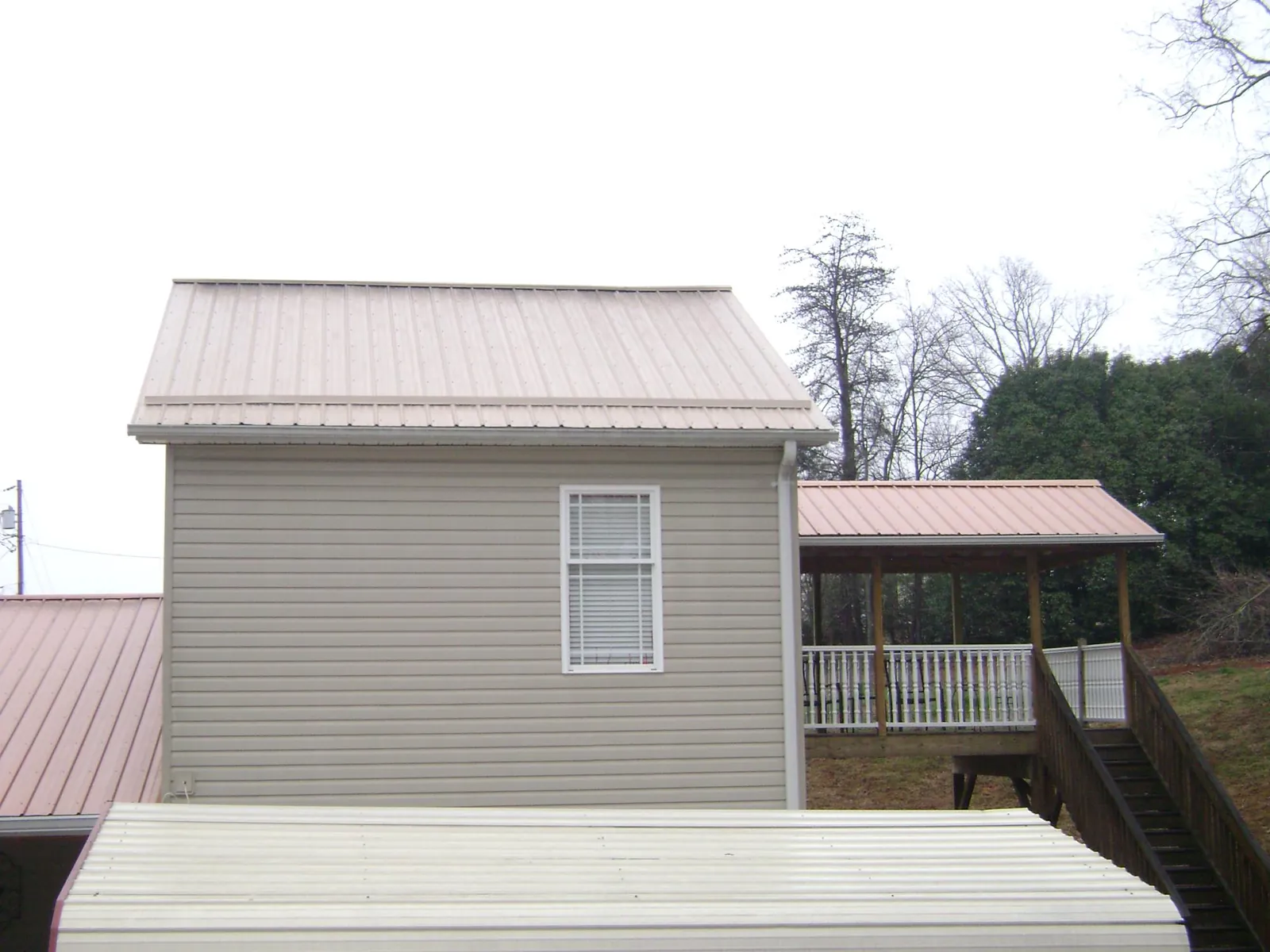 Tan metal roofs on a two story addition and attached porch, from a Roof Replacement job in Lancing